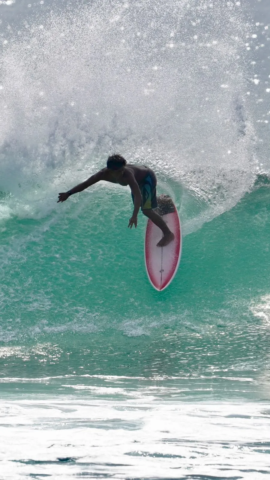 West Surf Lombok's coach dropping into a wave on a pink surfboard, spray behind him.